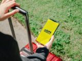 A person holds a smartphone showing an eSIM app while standing with luggage outdoors in Los Angeles.