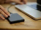 Close-up of a person connecting an external hard drive to a laptop on a desk.
