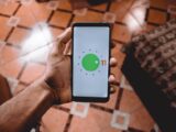 Close-up of a hand holding a smartphone displaying Android 11 interface indoors on patterned floor.