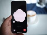 Close-up of a smartphone in hand with AI voice chat bubble and coffee in background.