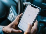 Close-up of hands holding a smartphone with GPS navigation displayed, in a car setting.