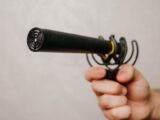 Hand holding a shotgun microphone with foam cover, ideal for voice recording and audio capture.