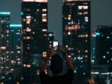 A person photographing Jakarta's illuminated skyscrapers during a vibrant city night.