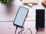 Smartphone charging with a power bank on a wooden desk, showcasing modern technology essentials.