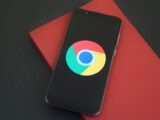 Close-up of a smartphone with Chrome browser logo on screen placed on a red notebook.