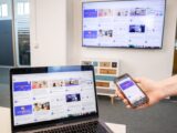 Digital devices including a laptop, phone, and TV in a modern office setting showing content synchronization.