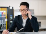 Adult man in a suit talking on mobile phone while taking notes in an office setting.