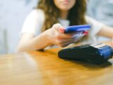 A woman processes a contactless payment using her smartphone at a payment terminal.