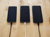 Three smartphones connected to chargers on a wooden surface, showcasing modern technology