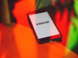 A smartphone displaying an 'ERROR' message surrounded by vibrant red and green reflections indoors.