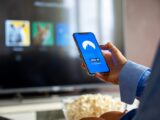 Person using VPN on smartphone while watching smart TV at home.