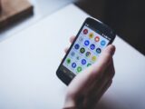 Close-up of a person holding a smartphone with various app icons visible on the screen.