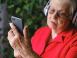 Senior woman in red using smartphone with headphones outdoors.