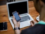 person holding black iPhone 4 front of MacBook Air