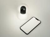 A smart home security camera paired with a blank smartphone on a white background.