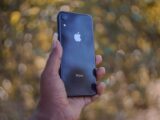 A close-up of a hand holding a smartphone with a blurred outdoor background.