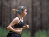 A young woman jogging through nature, listening to music with headphones.