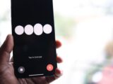 Close-up of a smartphone screen displaying a 'Tap to interrupt' prompt held in a hand.
