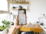 Hand holding smartphone indoors with blurred office background, focus on screen notifications.