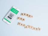 Smartphone displaying COVID-19 health passport next to Scrabble letters spelling 'Ready for Vacations' on a pastel background.