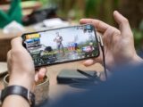 Person playing PUBG on smartphone outdoors with charging cable attached.