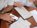 Senior couple examining bills and documents with smartphone and clipboard at home.