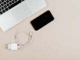 Flat lay of a laptop, smartphone, and charger on a beige background showcasing modern technology essentials.