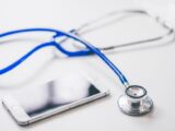 A smartphone and blue stethoscope on a clean white surface, emphasizing modern healthcare.