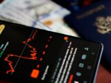Close-up of a smartphone displaying a stock market app alongside a US passport and currency.