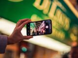 A person takes a vibrant city street photo with a smartphone at night, showcasing technology's role in modern photography.