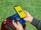 Hands holding a smartphone with eSIM and a passport near a luggage outdoors, ideal for travel concepts.