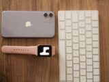 Flat lay of smartphone, smartwatch, and keyboard on a wooden desk, showcasing modern tech accessories.