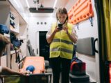 Female paramedic using smartphone inside an ambulance preparing for emergency response.