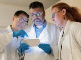 three people in lab coats looking at a tablet