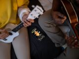 Top view of two people playing guitars using a smartphone app to learn chords.