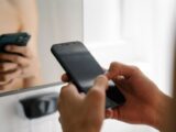 Crop unrecognizable person standing and using modern smartphone in light room in daytime