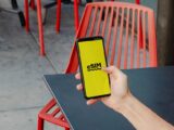 A person holding a smartphone displaying eSIM app screen, outdoors by red chair.