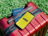Close-up of a red suitcase with a smartphone displaying eSIM and a passport, symbolizing travel readiness.