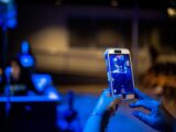Close-up of hands capturing a scene with a smartphone in a dimly lit environment.