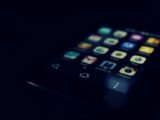 Dark-themed close-up of a smartphone screen highlighting various apps and touchscreen technology.