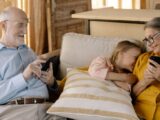 A warm family moment with grandparents and granddaughter using smartphones on a cozy sofa.