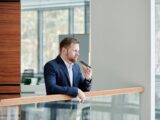 Professional businessman holding a smartphone and speaking indoors at a modern office setting.