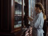 A female pharmacist in a white uniform organizing bottles in a pharmacy cabinet.