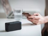 Person connecting a smartphone to a wireless speaker indoors, foreground focus.