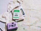 Flat lay of travel essentials including a passport, map, smartphone, and pop camera.