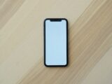 A black smartphone with a blank white screen on a light wooden surface