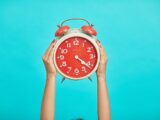 person holding red and beige twin bell analog alarm clock